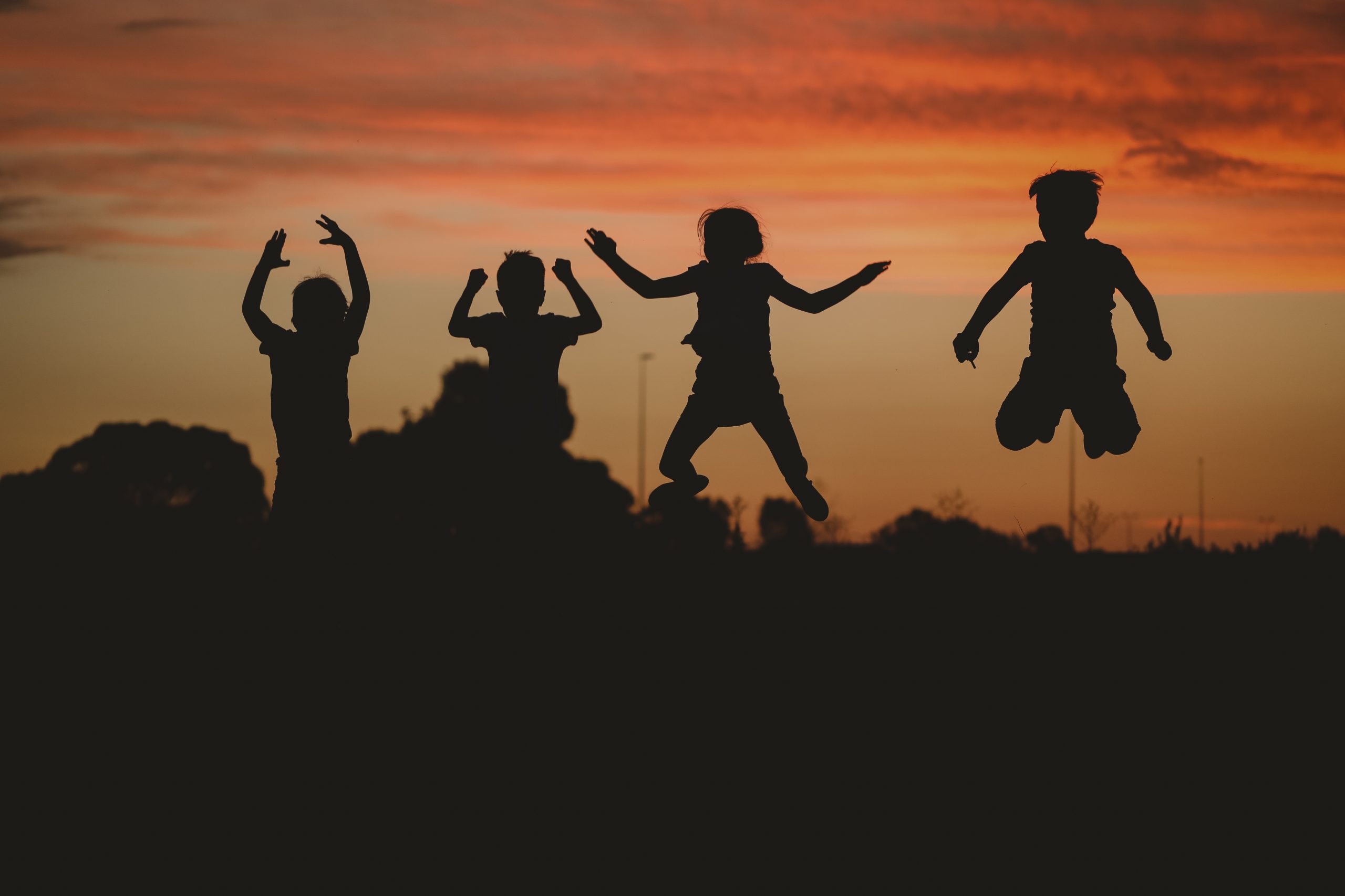 The silhouette of children posing on the hill surrounded by greenery during a golden sunset